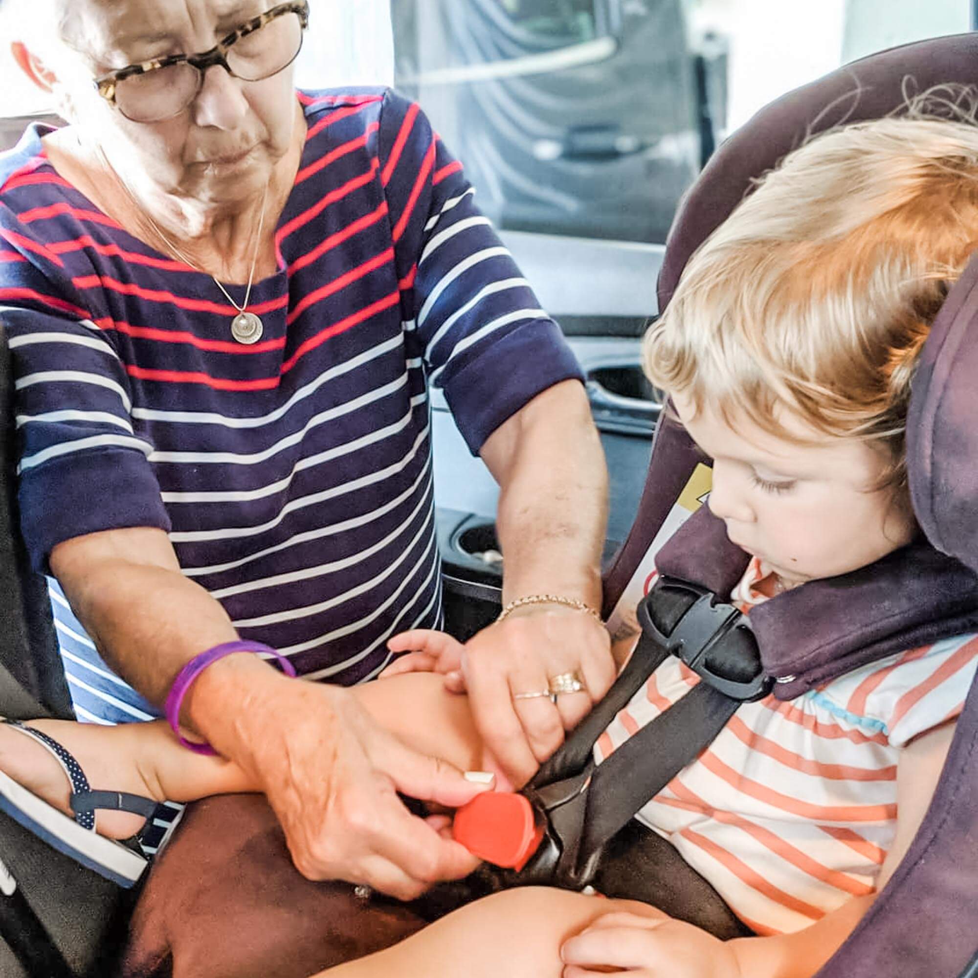 Photo of a grandma using UnbuckleMe to open her grandson's car seat buckle while he is watching her