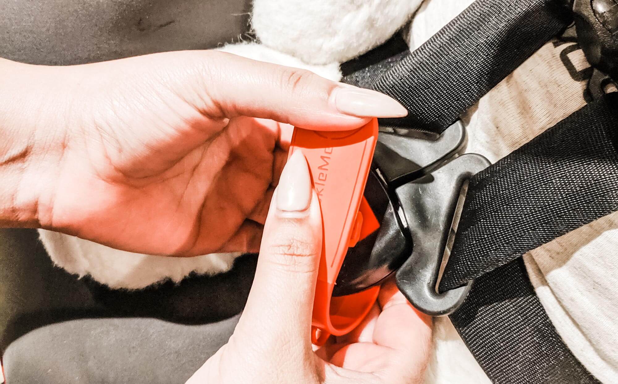 Photo of hands with long fingernails using UnbuckleMe to open a car seat buckle